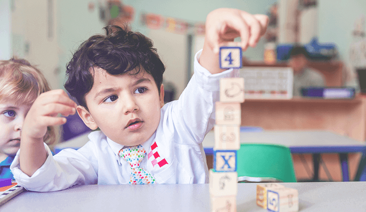 a boy puts a wooden block on top of a tower of other wooden blocks on a table in a French preschool in New York