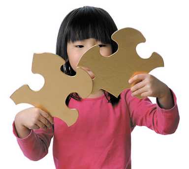 A young girl with dark hair and a pink shirt holding two large, gold-colored puzzle pieces together.