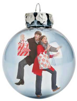 A silver Christmas ornament reflecting a man and woman in winter coats looking panicked while carrying holiday shopping bags.