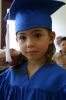 A young child in a blue graduation cap and gown looks directly at the camera with a slight, proud smile.