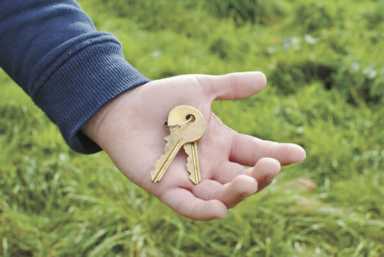 A person’s open palm holding two brass keys on a ring, set against a soft-focus background of green grass.