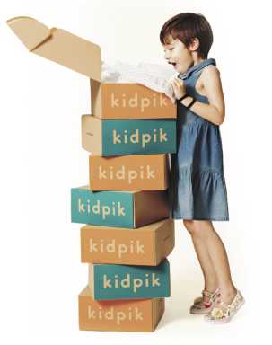 A young girl in a blue dress looks excitedly into an open box on top of a tall stack of "kidpik" subscription boxes.