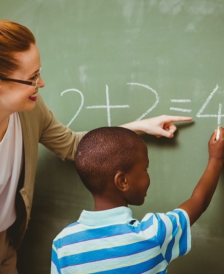 Teacher assisting boy to write on blackboard in classroom