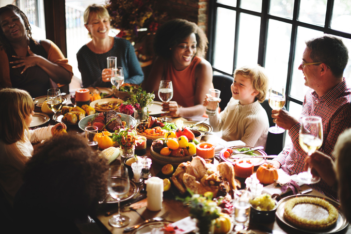 A diverse group of family and friends smile and toast with drinks around a large table filled with a festive feast.