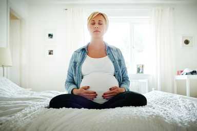 Pregnant woman meditating on bed