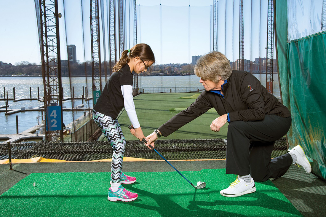 instructor showing girl how to hit golf ball