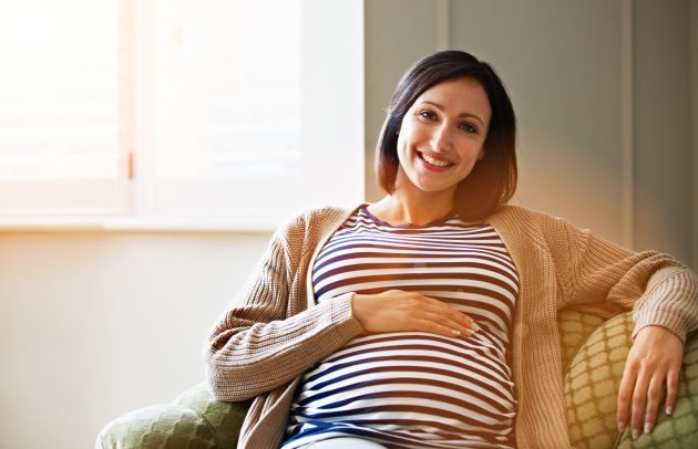 Portrait of a smiling pregnant woman sitting on her sofa