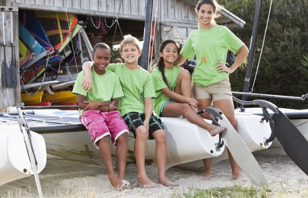 Teenage camp counselor with children sitting on catamaran at water sports equipment rental shack.