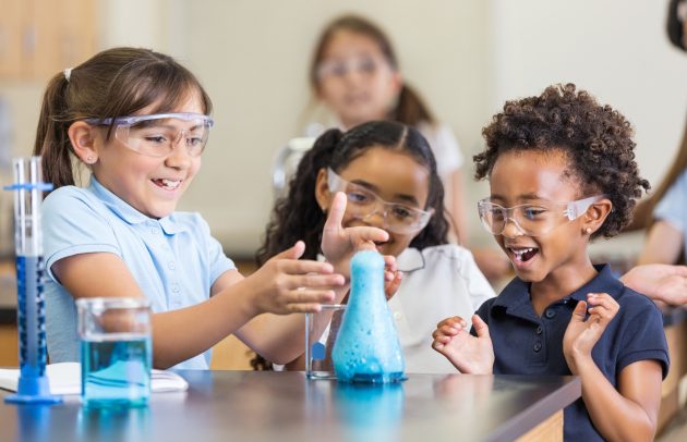 Excited girls using chemistry set together in elementary science classroom