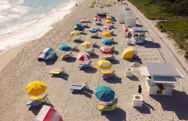 aerial photo of beach with ulti-colored beach umbrellas and chairs alongside waves and sand