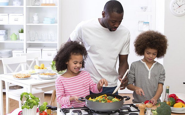 Dad cooking a healthy meal with his two young daughters in a brightly lit kitchen