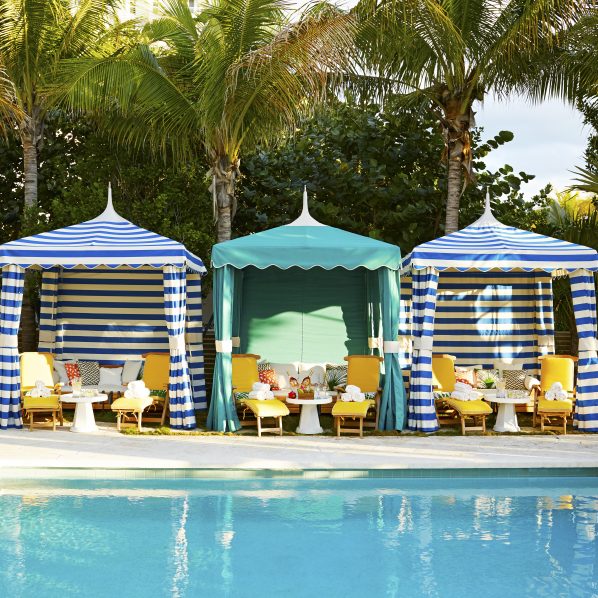 three cabanas with striped awnings and beach chairs, set up next to pool at fancy resort