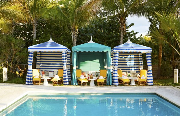 three cabanas with striped awnings and beach chairs, set up next to pool at fancy resort