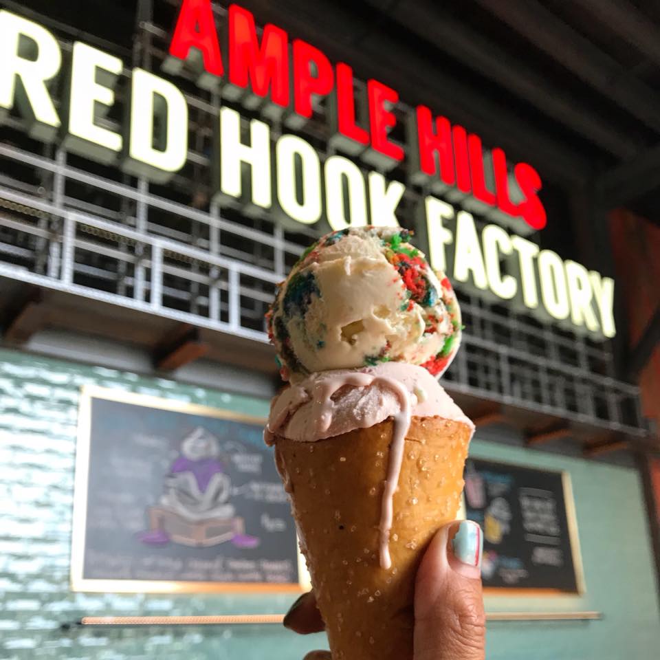 ice cream cone held up in front of a sign announcing the ample hill red hook ice cream factory