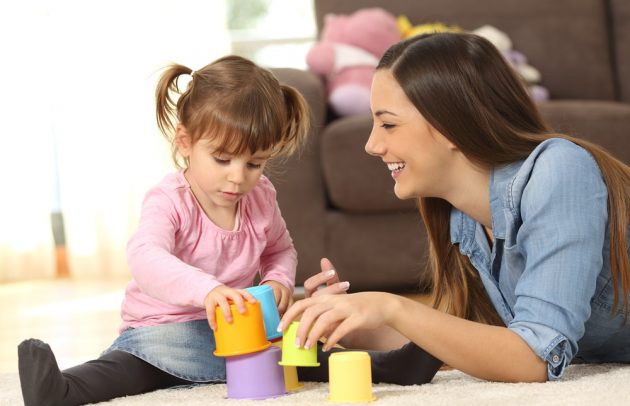 babysitter and child playing with colorful toys on the floor