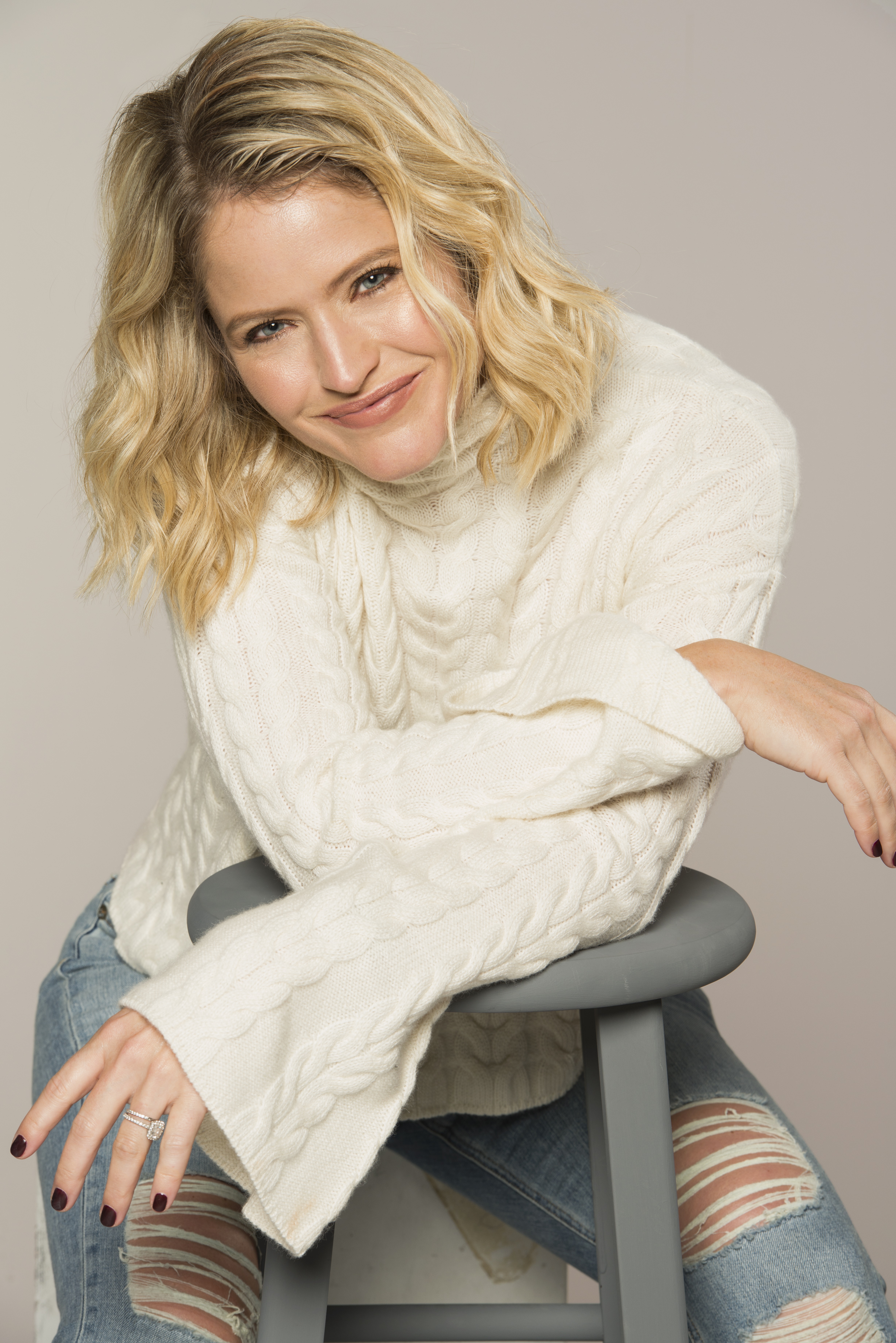 sara haines in white sweater and jeans leaning on stool