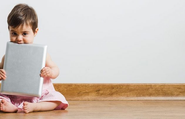 toddler holding ipad sitting on wood floor