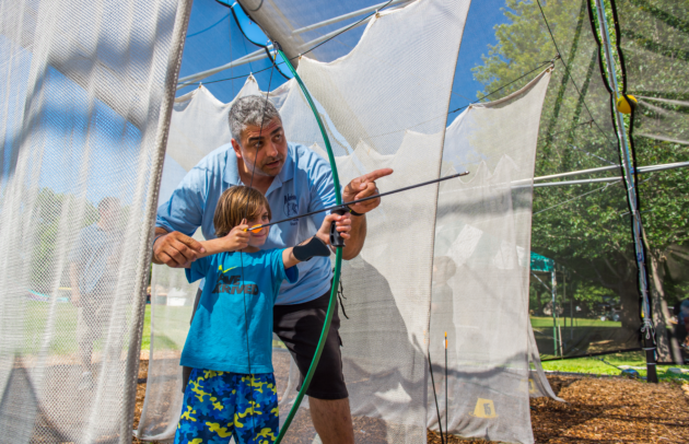 young boy getting bow and arrow instruction at camp from an adult counselor