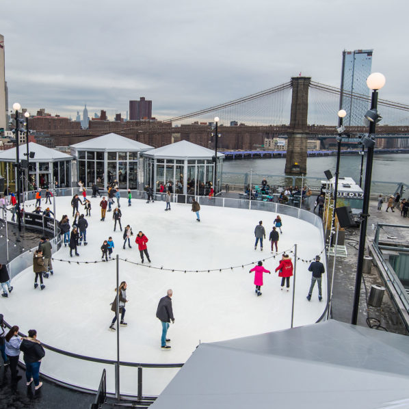 skaters on a rooftop ice rink with the brooklyn bridge in the background