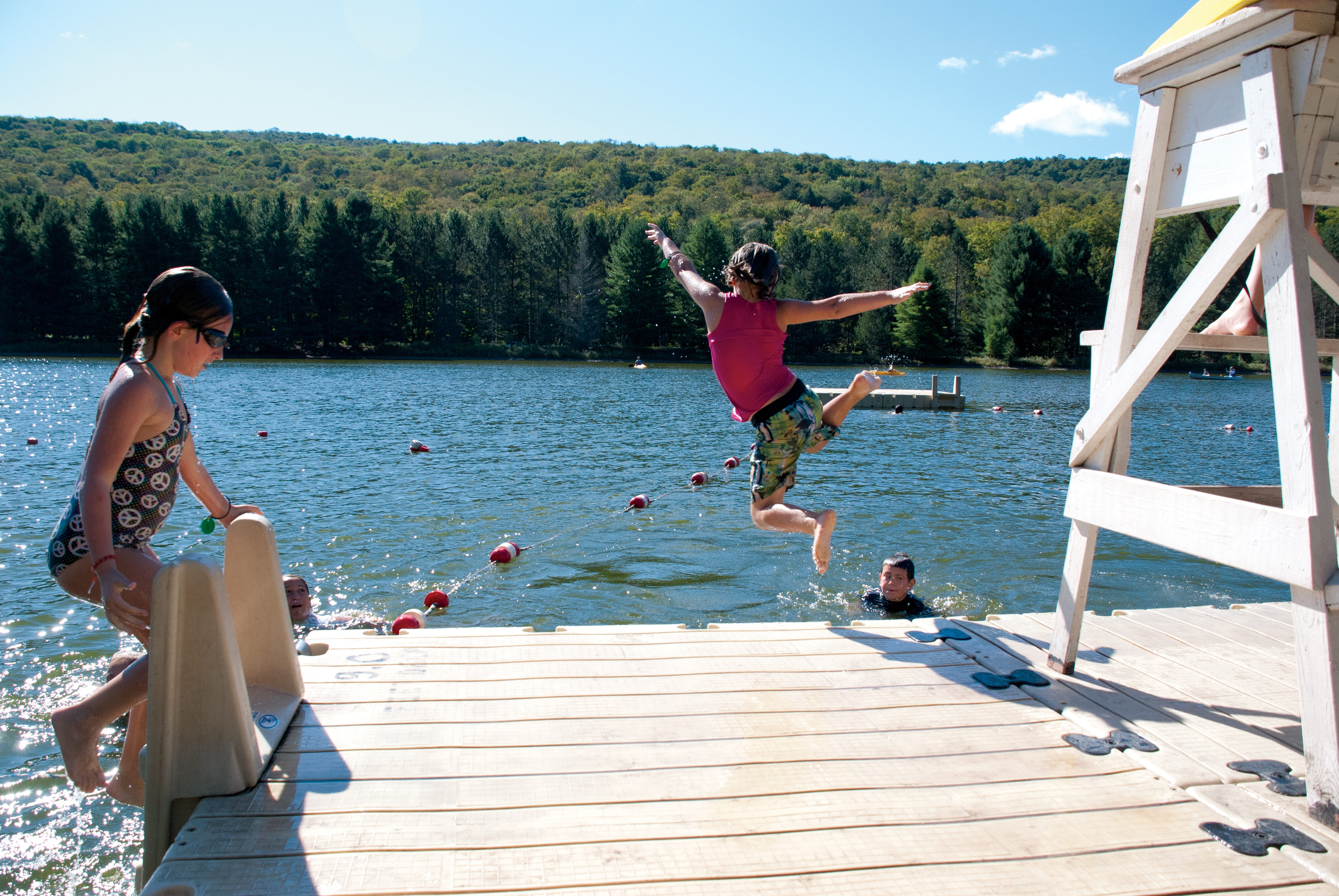 camper jumping into a lake from a dock at summer camp