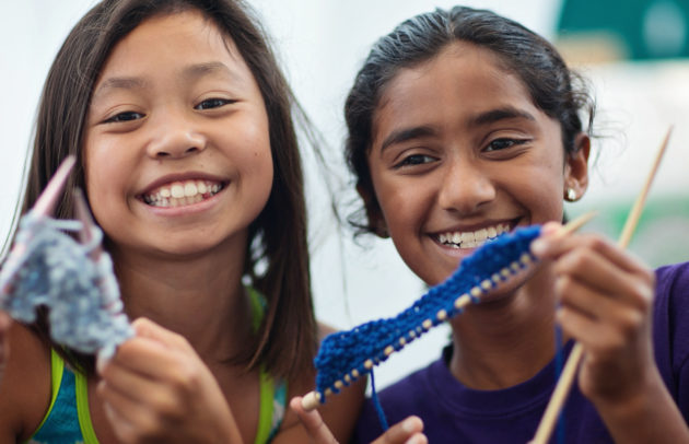 two young girls at summer camp doing a knitting activity