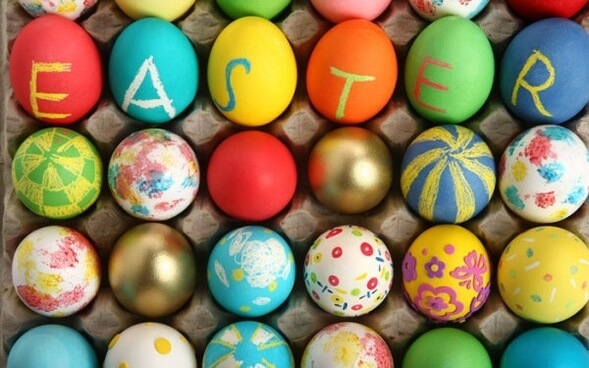 Colored and decorated Easter eggs in brown carton with Easter spelled across on some of the eggs