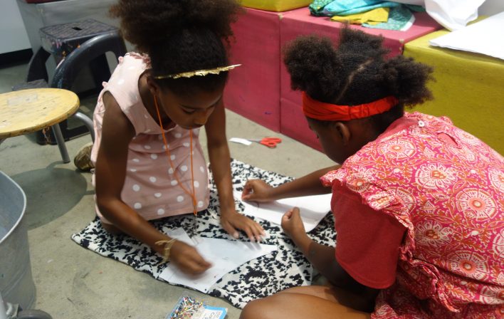 two girls put pushpins through paper onto black and white fabric