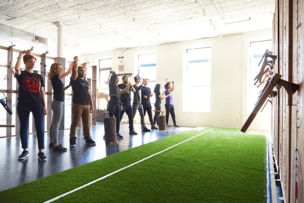 a group of people holds axes over their heads as they prepare to throw them at targets on a wooden wall