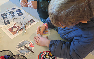 a child colors with a picture of a rocket and printouts of space on the table near him