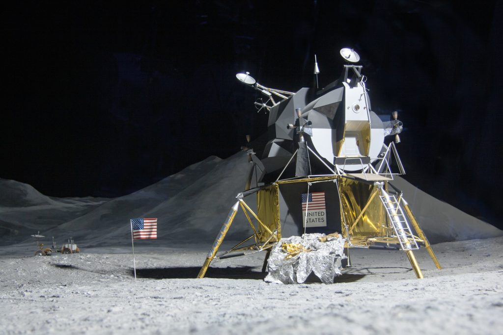 a lunar module sits on the moon next to an American flag