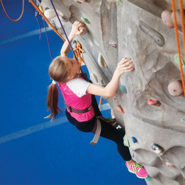 girl in pink shirt climbs gray rock wall