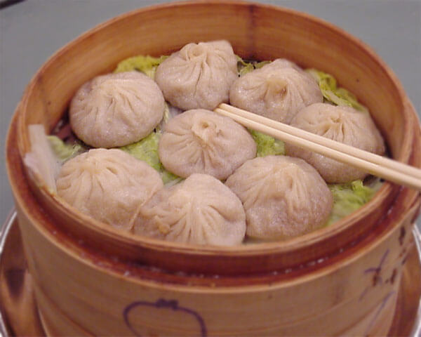 eight dumplings sit on a bed of cabbage in a bamboo steamer with chopsticks