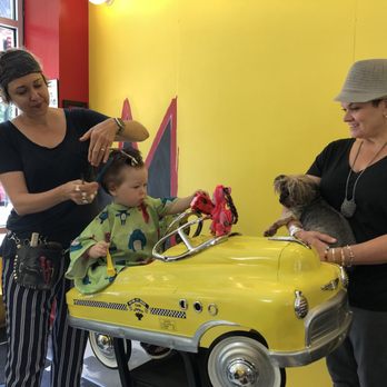 The image titled "348s.jpg" shows a child getting a haircut while sitting in a yellow toy car, with one adult styling and another holding a small dog.