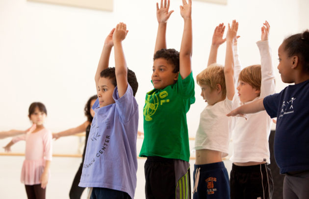 boys raise their arms up as they stand in a dance studio