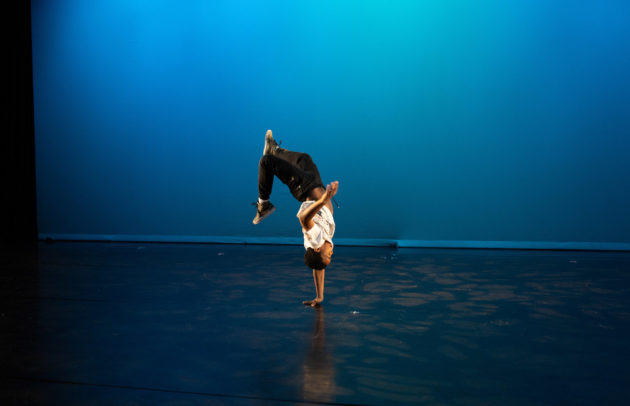a boy does a handstand on a stage with a blue background