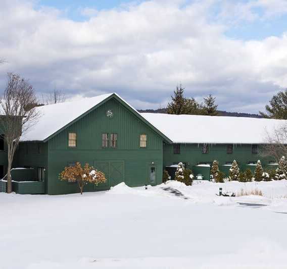 Green building with snowy roof surrounded by white winter landscape, cloudy sky, and pine trees, evokes peacefulness and serenity.