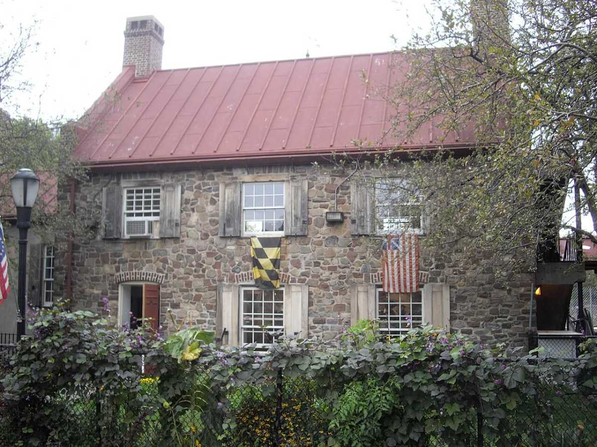 The file "fp-family-day-out-Old-stone-house-brooklyn-2019-12-1200x900.jpg" shows a two-story stone house with a reddish roof, shuttered windows, colonial-era flags, and a garden in front, partially obscured by leafy branches.
