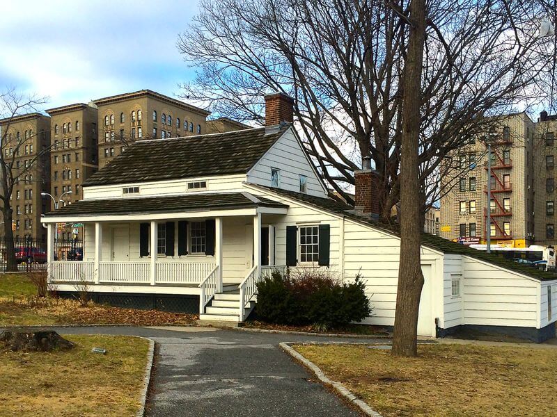 The file "fp-family-day-out-edgar-allan-poe-cottage-bronx-photo-cred-the-smithsonian-magazine-2019-12-568x568.jpg" shows a small historic white wooden cottage with a porch, black shutters, and sloped roof, set among trees and city buildings.