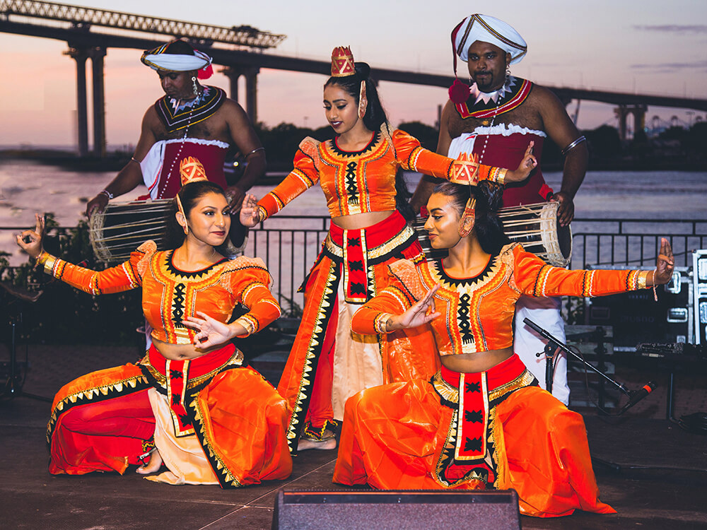 three women and two men dance in orange and red dress 