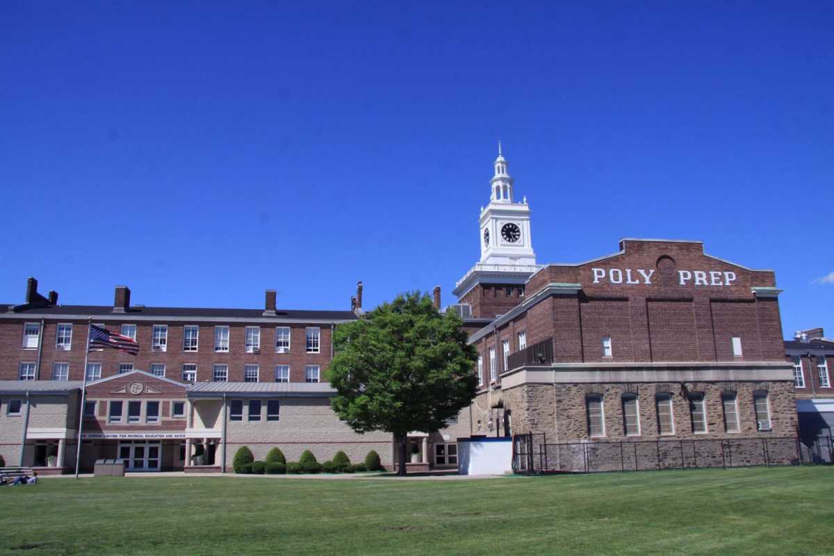 A large brick school building with a clock tower and the words "POLY PREP" on one side. The building is surrounded by a grassy field under a clear blue sky.