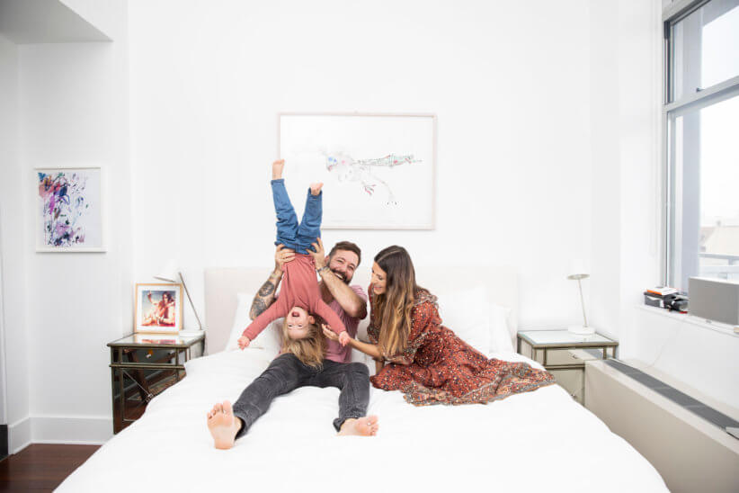 family sitting on bed and holding child upside down