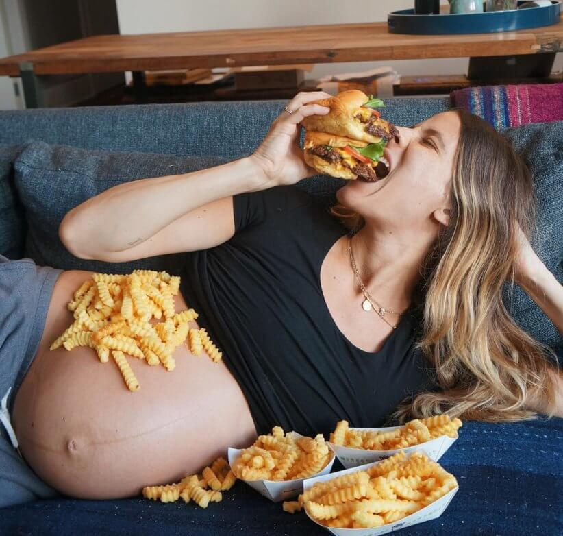 Eden Grinshpan pregnant and eating a hamburger on coach
