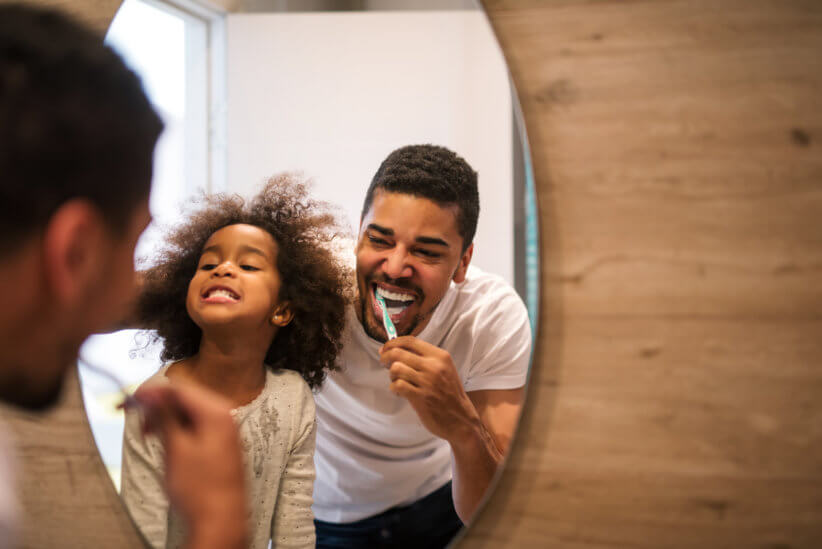 father and daughter brushing teeth in front of the mirror