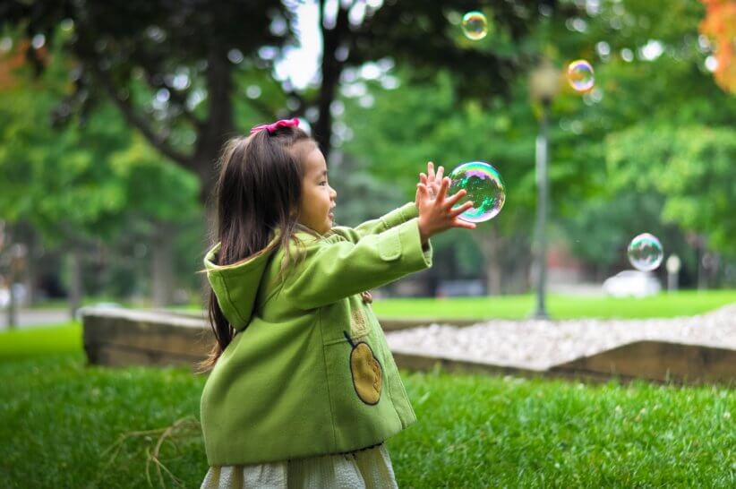 girl wearing green jacket playing with bubbles