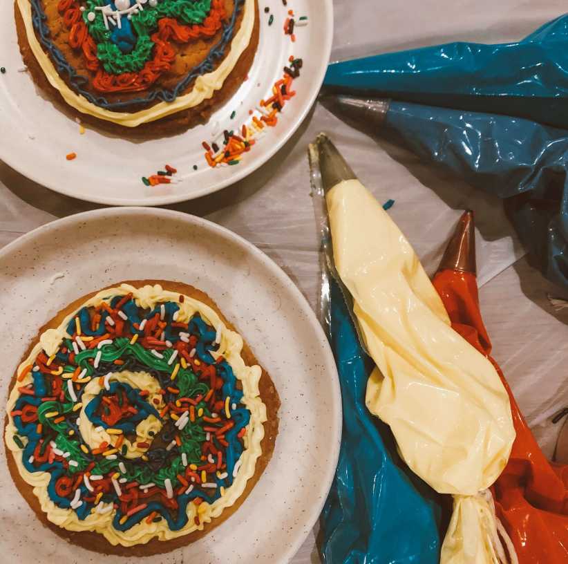Overhead view of two large cookies decorated with colorful icing and sprinkles next to piping bags.