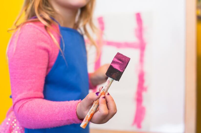 child with paint brush and pink paint