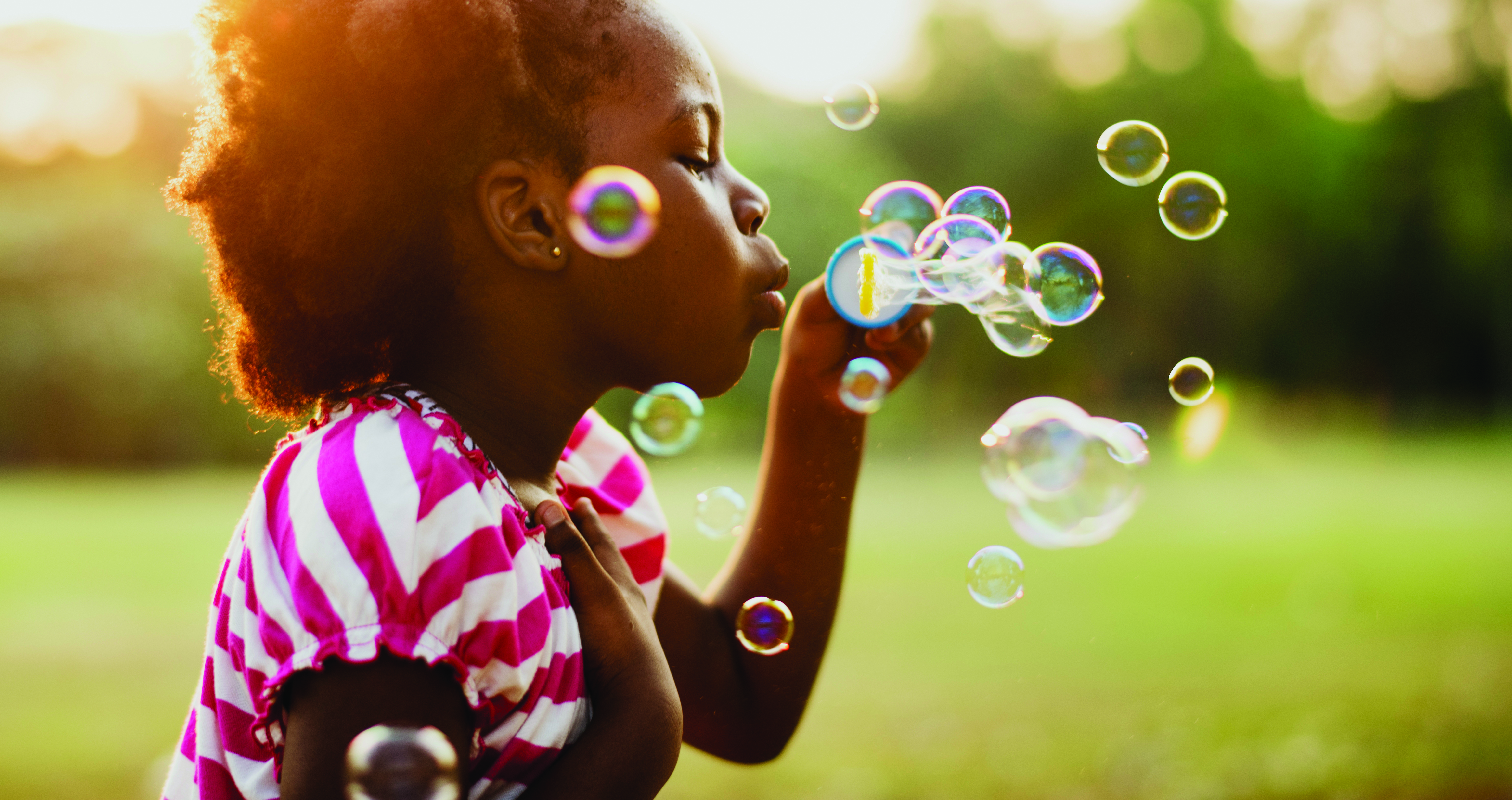 African descent girl playing blowing bubble in a park
