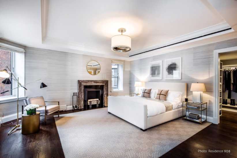 Spacious bedroom with a modern chandelier, fireplace, white bed, neutral decor, sitting area, and walk-in closet access.