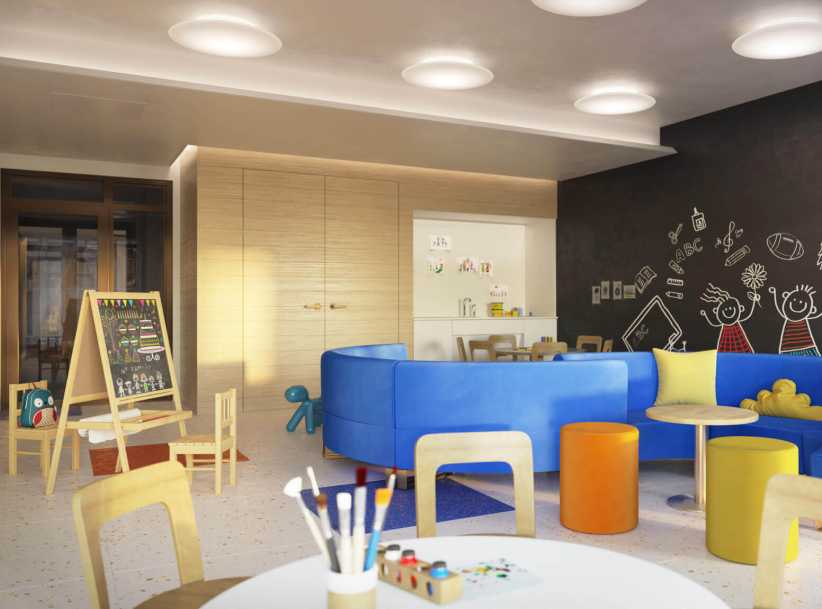 
Colorful children’s playroom with blue couches, small tables, an art easel, bright chairs, and a wall decorated with cheerful chalk drawings.