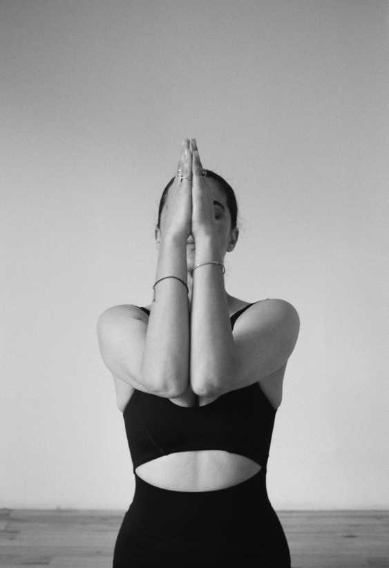 A black-and-white portrait of a woman with her palms pressed together and elbows touching in front of her face.